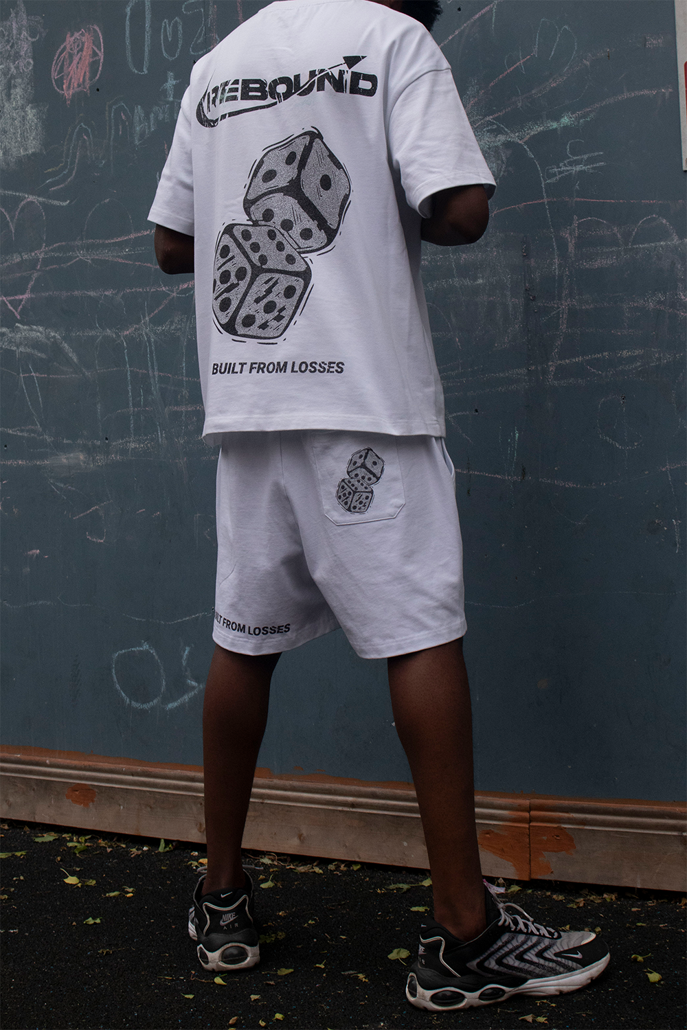 Rebound streetwear model in clean white tee standing confidently in front of blue urban wall