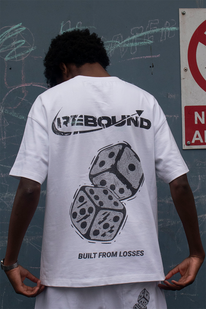 Person wearing a rebound white t-shirt with graphics and text, standing next to a 'No Dogs Allowed' sign on a dark wall.